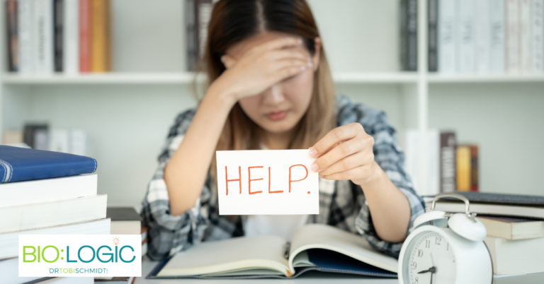 Frustrated girl sitting at desk studying holding up a "help" sign.